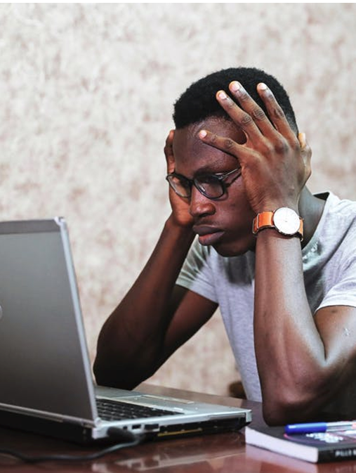 A man looks stressed out as he grips his head while staring at a computer screen. 